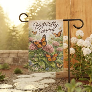 Puede incluir: Una bandera de jardín con una ilustración de mariposas monarca y flores rosas. El texto "Butterfly Garden" está escrito en la bandera. Se presenta en un soporte de metal negro, evocando la naturaleza y la tranquilidad.