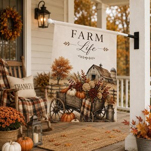 May include: A rectangular garden flag featuring the text FARM Life in black lettering. The illustration depicts a wooden wagon filled with pumpkins and autumn flowers, positioned in front of a rustic barn, a silo, and a tree with orange leaves.