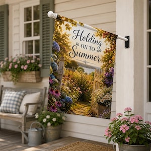 May include: A rectangular garden flag featuring a sunlit path through a flower garden with blue hydrangeas, purple coneflowers, and white daisies. The text "Holding ON TO Summer" is printed in black script and serif font in the upper center.