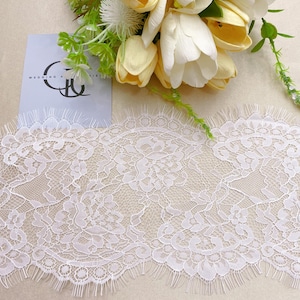May include: A close-up of white lace trim with a floral design and a scalloped edge. A bouquet of white and yellow tulips and greenery is in the background. A card with the text "WEDDING" is also visible.