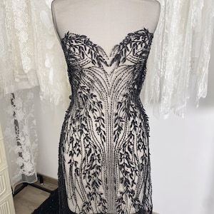 May include: A black lace bodice with a sweetheart neckline and detailed leaf embroidery. The design is displayed on a mannequin, highlighting the intricate pattern and texture of the fabric. The garment appears to be part of a formal dress or bridal wear.