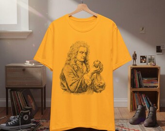 May include: Mustard yellow t-shirt featuring a black and white illustration of Isaac Newton holding an apple. The graphic is centered on the front of the shirt. The shirt is hanging on a wooden hanger.