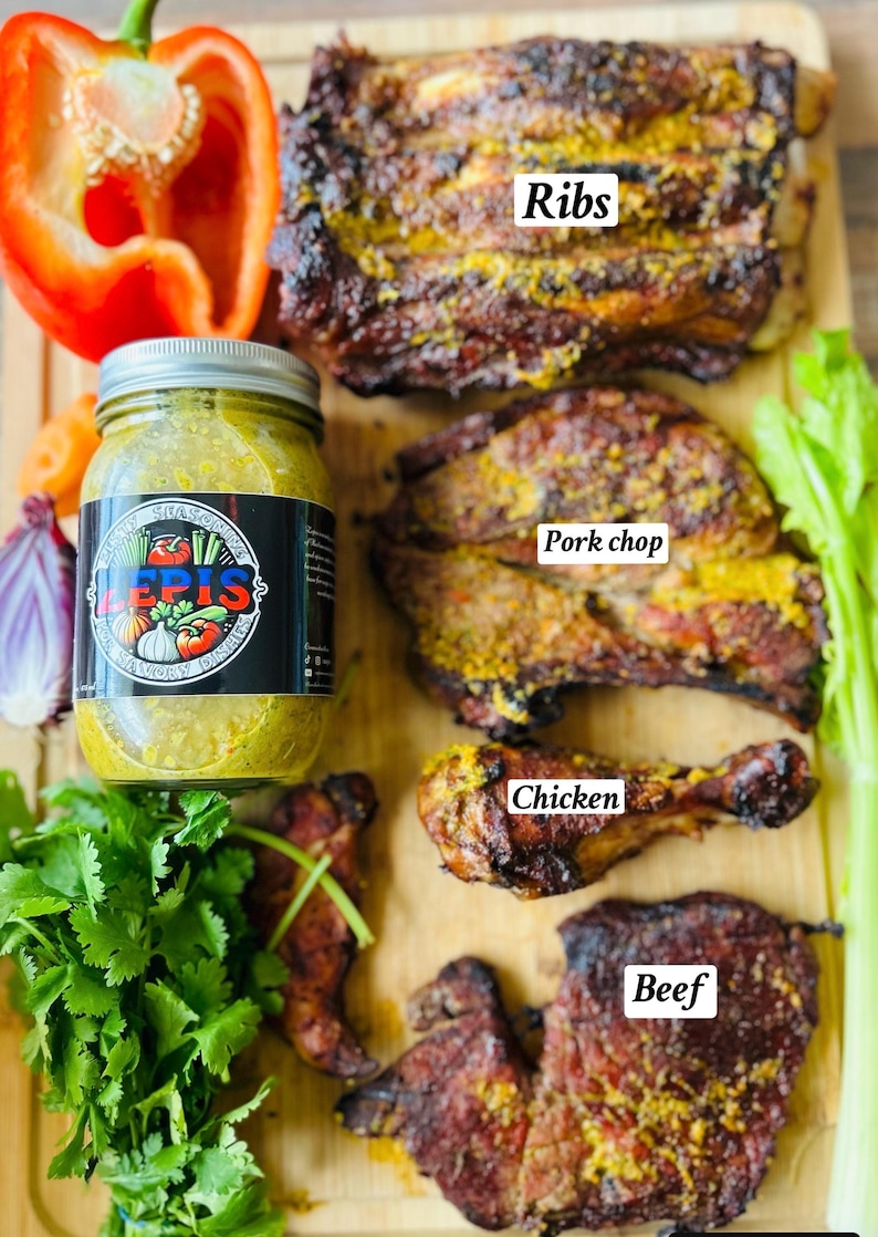 May include: A wooden cutting board with various types of meat, including ribs, pork chop, chicken, and beef. The meat is seasoned with a yellow spice and is ready to be served. There is a jar of green sauce and a red bell pepper on the board.