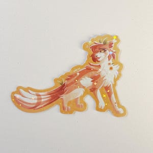 May include: A die-cut sticker featuring a stylized orange and white feline character with a long, bushy tail. The illustration includes small floral accents on the chest and head, finished with a holographic star pattern overlaying the design.