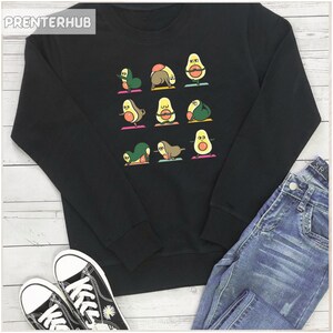 Könnte beinhalten: Schwarzes Sweatshirt mit einem Aufdruck von Avocados, die Yoga-Posen einnehmen. Die Avocados sind grün mit braunen Kernen und haben lächelnde Gesichter. Der Text "PRENTERHUB" befindet sich in der oberen linken Ecke des Sweatshirts.