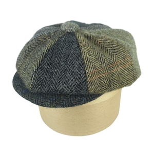Puede incluir: Una gorra de estilo newsboy de varios paneles con un diseño de patchwork de diversos tejidos de mezcla de lana. La gorra muestra una mezcla de tonos gris carbón, verde oliva y marrón, con un patrón de espiga y un botón central de tela.
