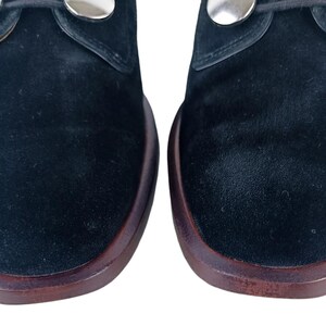 May include: A pair of black suede shoes with silver metal accents. The shoes have a rounded toe and a low heel.
