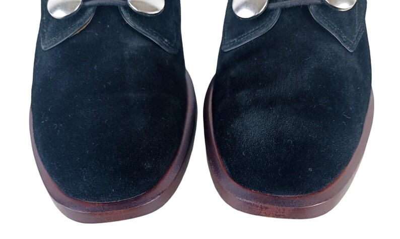 May include: A pair of black suede shoes with silver metal accents. The shoes have a rounded toe and a low heel.