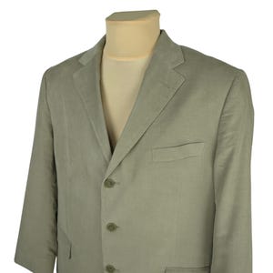 May include: A light green blazer with a three-button closure and a notched lapel. The blazer has a chest pocket and two lower pockets. The fabric has a subtle vertical texture. The blazer is displayed on a mannequin.