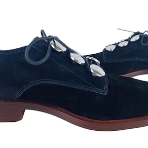 May include: Black suede lace-up shoes with silver metal accents. The shoes have a rounded toe and a low heel.