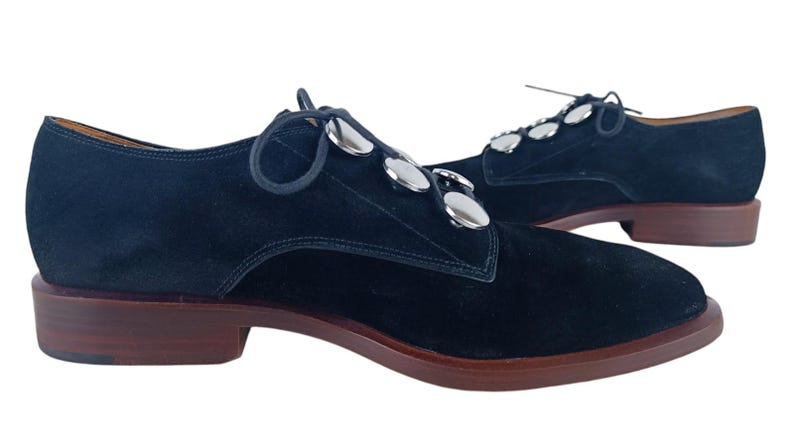 May include: Black suede lace-up shoes with silver metal accents. The shoes have a rounded toe and a low heel.
