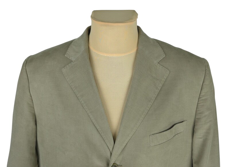 May include: A light green blazer with a notched lapel and a single-breasted design. The blazer has a chest pocket and is displayed on a mannequin. The fabric appears to be a lightweight material.