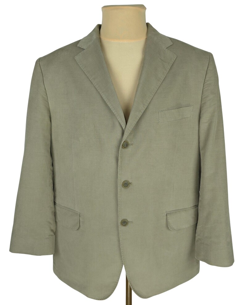 May include: A light green blazer with a three-button closure, a notched lapel, and two front pockets. The blazer is displayed on a mannequin and has a classic, tailored design. The fabric appears to be a lightweight material, suitable for warmer weather.