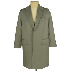 Puede incluir: Un abrigo verde salvia con solapa de muesca, dos bolsillos delanteros y un bolsillo en el pecho. El abrigo se exhibe en un maniquí y tiene un diseño clásico y a medida. El abrigo es de color liso y parece estar hecho de lana o mezcla de lana.