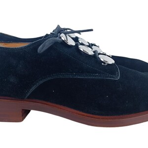 May include: Black suede lace-up shoes with silver metal accents on the laces.