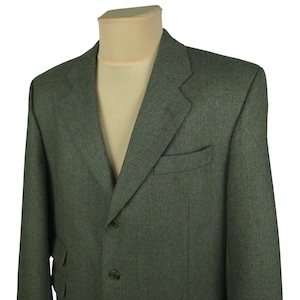 Op de afbeelding: Een groene visgraat blazer met twee knopen en een gekerfde revers. De jas heeft twee voorzakken en een borstzak. De blazer wordt getoond op een mannequin met een beige overhemd eronder.