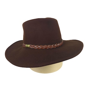 May include: A dark brown felt fedora hat featuring a wide brim and a pinched crown. The hat is accented with a braided brown leather band that wraps around the base of the crown, decorated with three small, metallic, brass-toned cylindrical beads.
