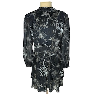Könnte beinhalten: Schwarzes Kleid mit floralem Muster. Das Kleid hat lange Ärmel, einen hohen Ausschnitt und einen Stufenrock. Das florale Design ist in Grau- und Weißtönen gehalten und erzeugt einen Kontrast zum schwarzen Stoff. Das Kleid ist aus leichtem Material.