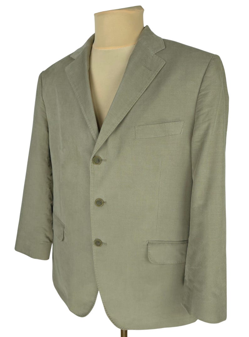 May include: A light green blazer with a three-button closure and notched lapels. The blazer has two front pockets and a chest pocket. The jacket is displayed on a mannequin.