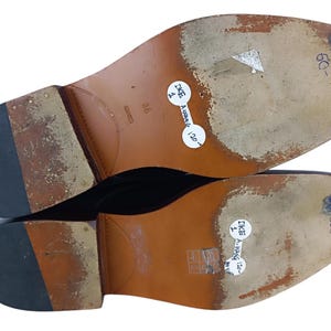 May include: Close-up of the soles of a pair of brown leather shoes. The soles are brown leather with a black rubber heel. The shoes are labelled "DKE" and "600".
