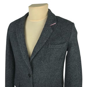 Puede incluir: Un blazer gris con cierre de un solo botón y solapa con muescas. El blazer tiene una tela texturizada y un acento rosa en la solapa. El blazer se muestra en un maniquí.