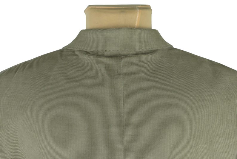 May include: Close-up of the back of a sage green corduroy jacket. The collar is visible, along with the textured fabric and vertical lines of the corduroy. The jacket is displayed on a mannequin.