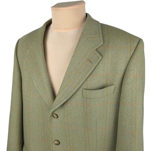 May include: A green tweed blazer with a subtle plaid pattern. The blazer has a notched lapel, a chest pocket, and two front pockets. It is displayed on a mannequin. The blazer has three buttons and a classic, tailored fit.
