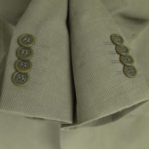 May include: Close-up of a tan corduroy blazer. The blazer features four matching buttons on each cuff. The fabric has a ribbed texture, and the buttons are a darker shade of tan.