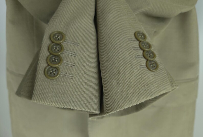 May include: Close-up of a tan corduroy blazer. The blazer features four matching buttons on each cuff. The fabric has a ribbed texture, and the buttons are a darker shade of tan.