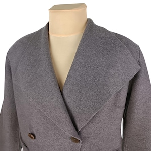 May include: A grey double-breasted coat with a wide lapel and two brown buttons. The coat is displayed on a mannequin. The coat's fabric appears to be a soft wool blend, suitable for cooler weather.
