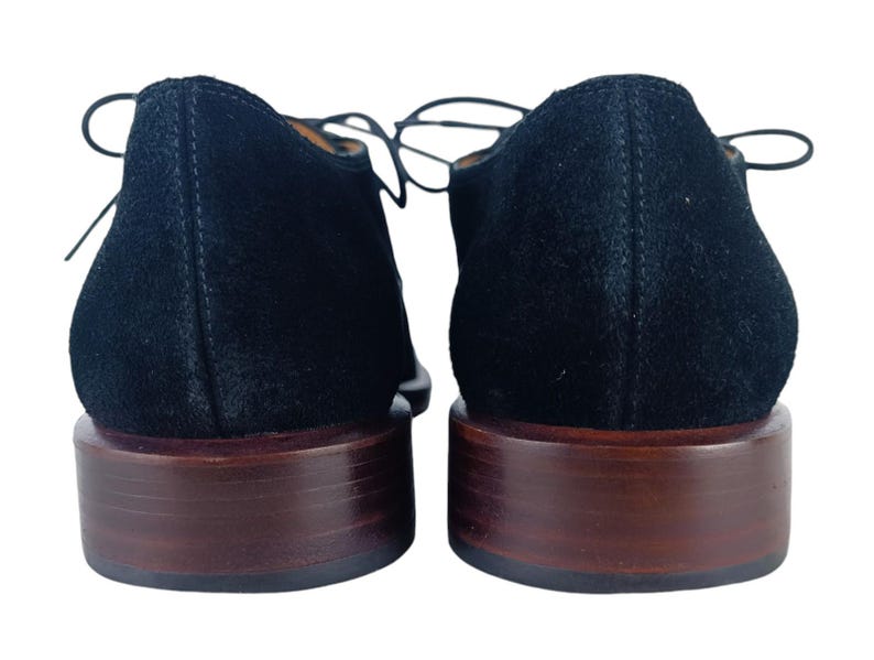 May include: A pair of black suede lace-up shoes with brown leather soles.