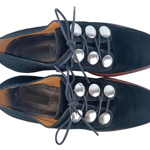 May include: Black suede lace-up shoes with silver metal accents. The shoes have a round toe and a low heel.