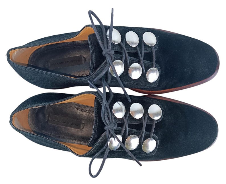 May include: Black suede lace-up shoes with silver metal accents. The shoes have a round toe and a low heel.