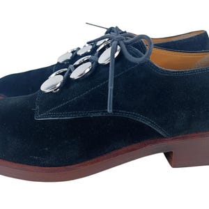 May include: Black suede lace-up shoes with silver metal accents on the laces.