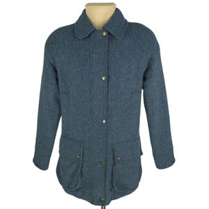 May include: A blue herringbone-patterned jacket with a classic collar and four gold-colored buttons down the front. The jacket has two front pockets with buttoned flaps and long sleeves. The garment is displayed on a mannequin.