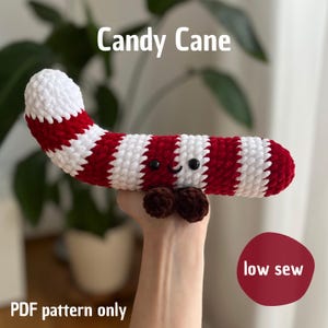 Puede incluir: Un bastón de caramelo de ganchillo con rayas rojas y blancas, ojos negros y una boca sonriente. El bastón de caramelo tiene una forma redondeada marrón en la parte inferior. El texto en la imagen dice "Candy Cane", "low sew" y "PDF pattern only".