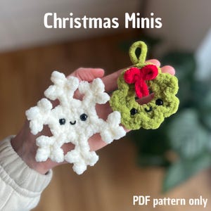 Könnte beinhalten: Zwei gehäkelte Weihnachtsdekorationen: eine weiße Schneeflocke und ein grüner Kranz mit roter Schleife. Beide haben lächelnde Gesichter mit schwarzen Augen. Der Text "Christmas Minis" steht oben und "PDF pattern only" unten.