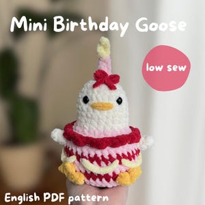 May include: A crocheted goose resembling a birthday cake, featuring a white body, a pink and red frilled skirt, a red bow, and a yellow beak. The image includes the text "Mini Birthday Goose" and "low sew".
