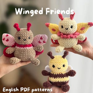 May include: Three handmade crochet winged creatures: a butterfly, a moth, and a bee. The butterfly is tan with pink and red wings. The moth is cream-colored with yellow and pink wings. The bee is yellow and brown. The text "Winged Friends" and "English PDF patterns" are visible.