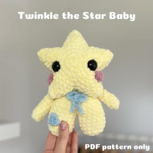 Könnte beinhalten: Ein gehäkeltes gelbes Stern-förmiges Babyspielzeug mit einer blauen Schleife und rosa Wangen. Das Spielzeug wird von einer Hand gehalten. Der Text "Twinkle the Star Baby" befindet sich oben im Bild und "PDF pattern only" unten im Bild.