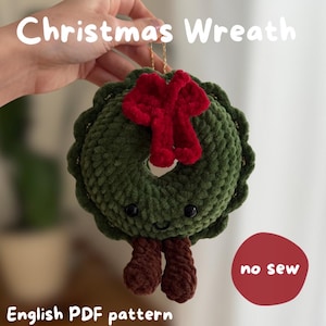 May include: A crocheted green Christmas wreath ornament with a red bow, two brown dangling legs, and a smiling face with black eyes. The text reads Christmas Wreath, no sew, and English PDF pattern.