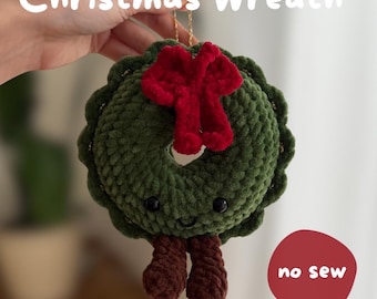 May include: A crocheted green Christmas wreath ornament with a red bow, two brown dangling legs, and a smiling face with black eyes. The text reads Christmas Wreath, no sew, and English PDF pattern.