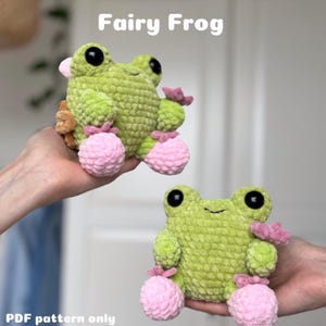 May include: Two crocheted green fairy frog plushies with pink feet and flower accents. The plushies are sitting on a hand. The text "Fairy Frog" is written in white on a light gray background. The text "PDF pattern only" is written in black on a white background.