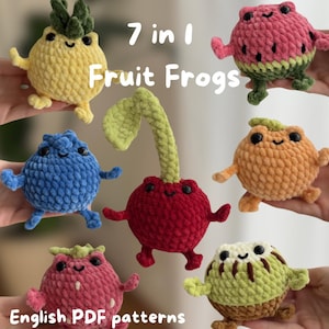 Könnte beinhalten: Sieben gehäkelte Plüschtiere in Froschform mit Fruchtdesign, darunter Ananas, Wassermelone, Blaubeere, Kirsche, Orange, Erdbeere und Kiwi. Jedes Tier hat schwarze Kunststoffaugen und ein gesticktes Lächeln. Text: 7 in 1 Fruit Frogs English PDF patterns.