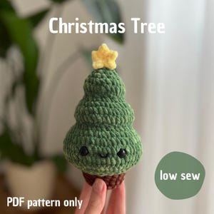 Könnte beinhalten: Ein grüner gehäkelter Weihnachtsbaum mit einem gelben Stern oben. Der Baum hat ein lächelndes Gesicht und steht auf einem braunen Sockel. Der Text auf dem Bild lautet "Christmas Tree", "PDF pattern only" und "low sew".
