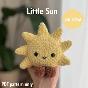 Puede incluir: Un peluche de sol amarillo tejido a ganchillo con ojos negros y una boca sonriente. El sol tiene rayos puntiagudos y dos pequeños pies marrones. El texto en la imagen dice "Little Sun", "no sew" y "PDF pattern only".
