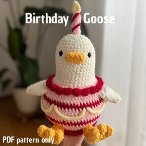 Könnte beinhalten: Ein gehäkeltes weißes Gänse-Plüschtier mit einem Geburtstagskuchen-Design. Die Gans hat einen gelben Schnabel und Füße, einen rot-rosa kuchenartigen Körper und eine Kerze auf dem Kopf. Der Text "Birthday Goose" und "PDF pattern only" sind sichtbar.