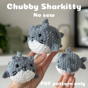 Könnte beinhalten: Drei gehäkelte Plüsch-Hai-Spielzeuge mit Katzenköpfen. Die Spielzeuge sind grau und weiß und haben ein nahtloses Design. Der Bildtext lautet "Chubby Sharkitty No sew PDF pattern only".