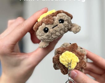 Puede incluir: Un llavero de rana pancake de crochet hecho con hilo marrón y amarillo. La rana está unida a un llavero de plata. El texto "Mini Pancake Frog" y "PDF pattern only" es visible en la imagen.