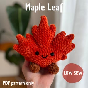 Könnte beinhalten: Ein gehäkeltes, orangefarbenes Ahornblatt-Spielzeug mit einem lächelnden Gesicht und kleinen braunen Füßen. Der Text "Maple Leaf" steht oben und "PDF pattern only" unten. Ein roter Kreis mit "LOW SEW" befindet sich rechts.